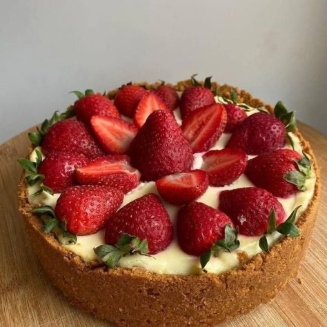A delicious homemade strawberry cheesecake with a golden graham cracker crust, topped with fresh, juicy strawberries, sitting on a wooden surface.